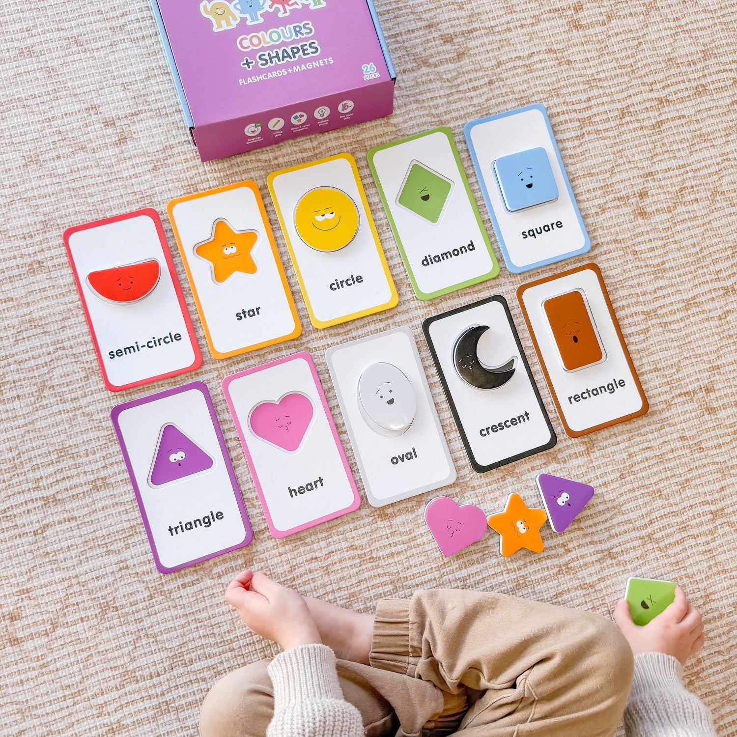 Educational card game with shapes and colours on a carpeted floor, child's hands visible.
